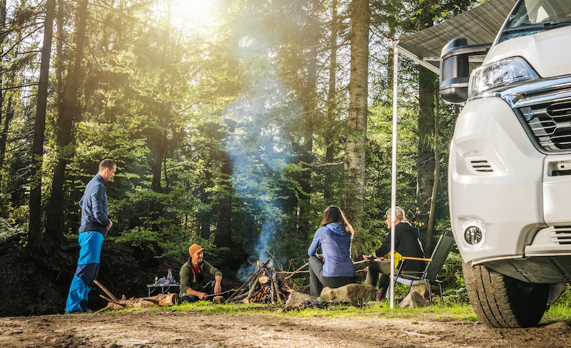 Four Adult Caucasian Friends in Their 40s Hanging Out Next to Campfire During Wilderness Boondocking Camper Camping