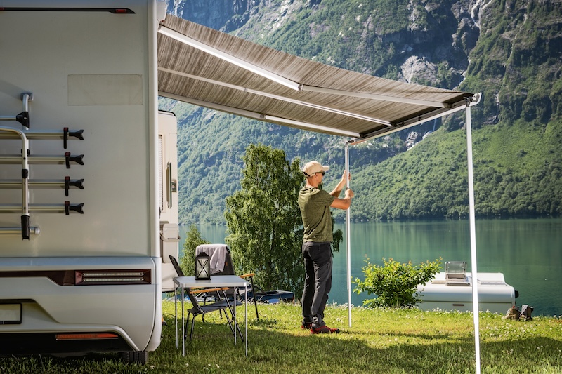 Caucasian Tourist Extending Camper Van RV Awning. Setting Up Scenic Campsite.