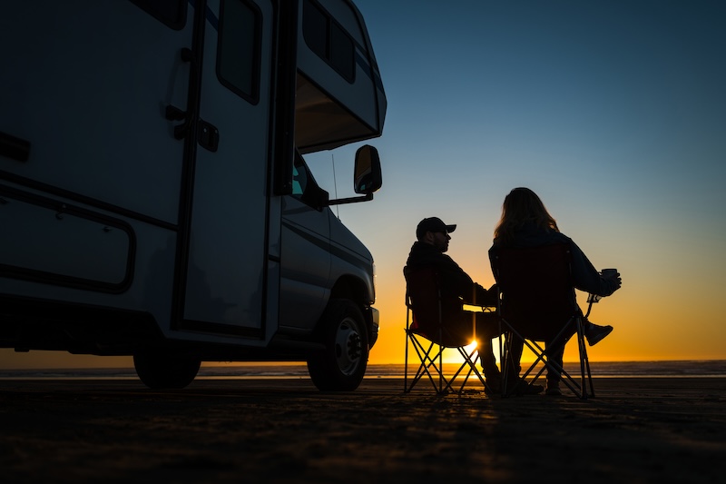 Caucasian Couple Relaxing Next to Their RV Motorhome on the Pismo Beach During Scenic Sunset. Recreational Vehicle Road Trip Theme.