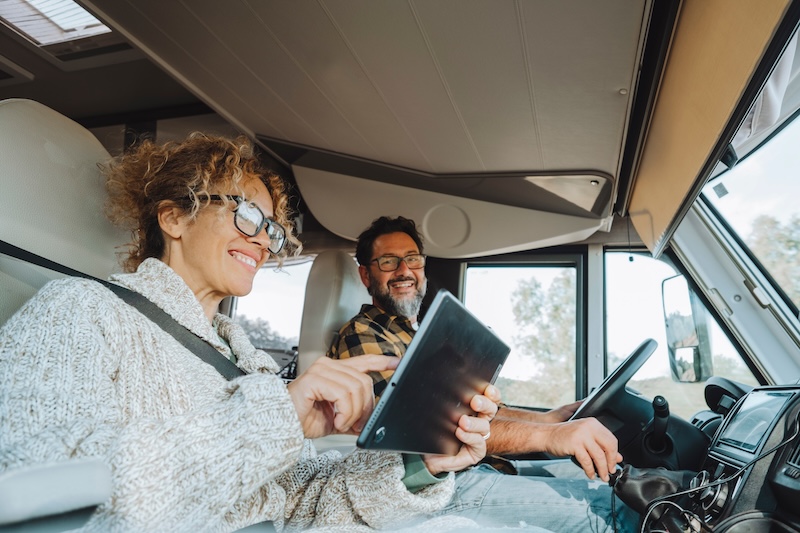 Happy couple of tourist traveler enjoy drive and live in camper van and using laptop to manage the road trip. Roaming connection during travel. Woman using device inside motorhome in vanlife together