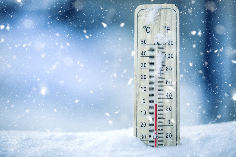 Thermometer on snow shows low temperatures in celsius or farenheit.