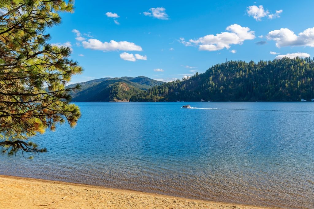 A boat passes in front of a small sandy beach at Beacon Point, a stop on the Centennial Trail, on lake Coeur d'Alene's Wolf Lodge Bay, in Coeur d'Alene, Idaho, USA.