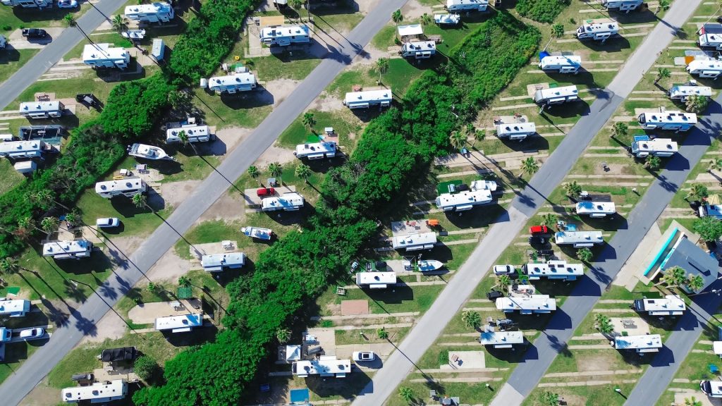 Campground office in large RV park campsite with long row of recreational vehicles and trailers boats tall palm trees in South Padre Island, aerial view campers basecamp with power hookup, Texas. USA